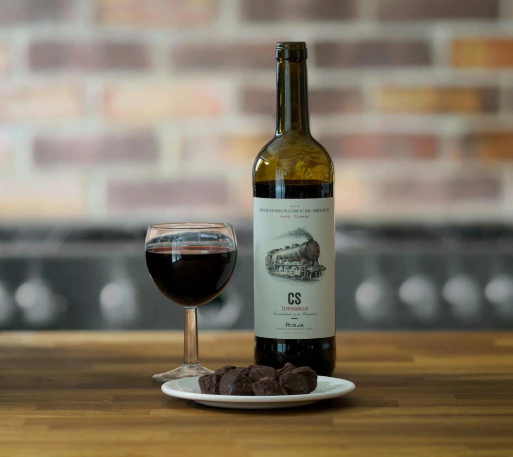 Wine and chocolate placed on an oak table with a blurred background.